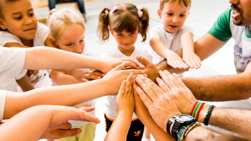 Kinder und Erwachsene legen ihre Hände in einem Kreis zusammen, symbolisieren Zusammenarbeit und Gemeinschaft.