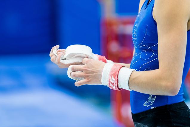 Nahaufnahme einer Sportlerin mit Kreide in der Hand, die ihre Hände mit einem roten Handgelenkschutz umwickelt.